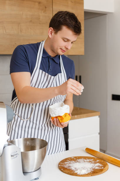 istock Young handsome man in apron sifting flour in modern kitchen 1319392016