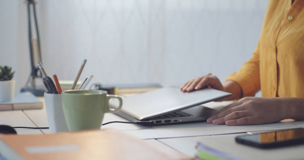 femme s’asseyant au bureau et utilisant son ordinateur portatif - closed photos et images de collection