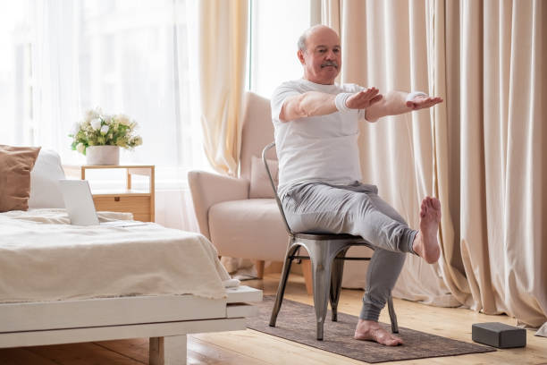starszy mężczyzna praktykujący jogę asana lub ćwiczenia sportowe na nogi i ręce na krześle - power chair zdjęcia i obrazy z banku zdjęć