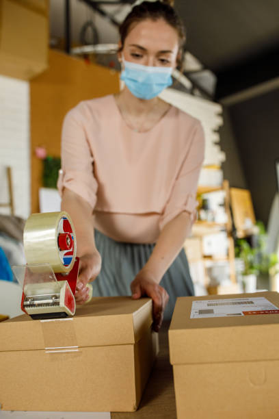 istock Young woman in a protective face mask taping a package 1319403233