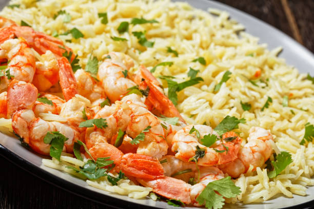 istock Mexican dish lime shrimps with cilantro and long grain rice cooked with chicken broth served on a plate on a dark wooden background, top view, close-up 1319407454