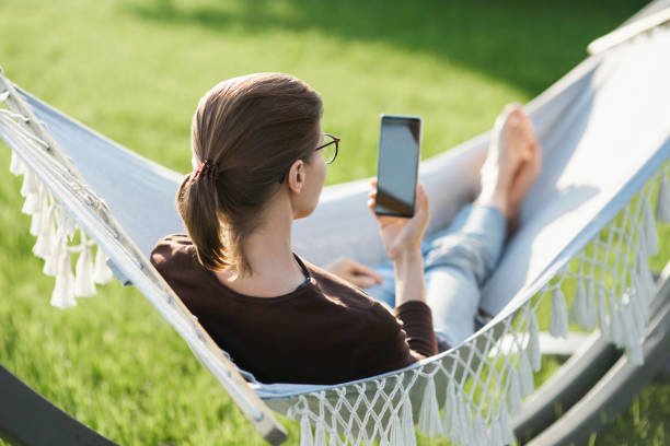 istock Young woman lying in a hammock using smartphone 1319408955
