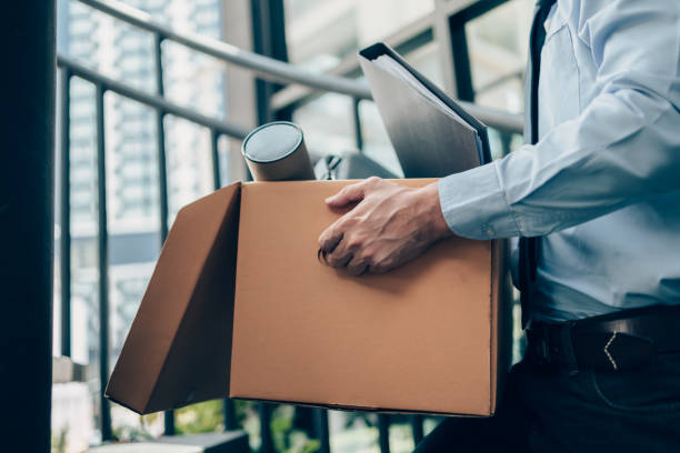 Unemployed hold cardboard box and laptop bag, dossier and drawing tube in box. Quitting a job, businessman fired or leave a job concept. stock photo