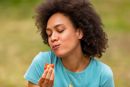 A Young Woman of African-American Ethnicity is Enjoying in Walking Through the Park and Eating Fresh Strawberries.