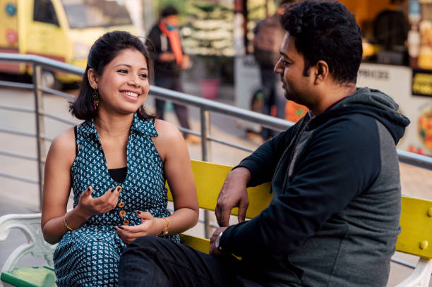 Romantic Indian couple sitting on bench and talking to each other Outdoor image of Romantic Indian couple sitting on bench and talking to each other outside a cafe in city at daytime. Concept of dating and meeting outside in cafeteria. men close up 20s asian ethnicity stock pictures, royalty-free photos & images