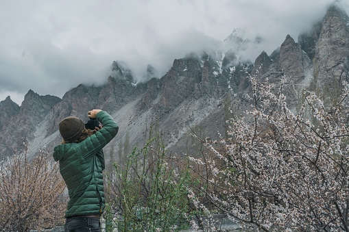 Young Caucasian man with camera  on the background of apricot blossom in northern Pakistan