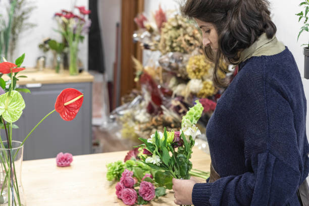 エプロン、若い女性起業家の概念を身に着けている彼女の花屋で緑と紫の花束を設計する女性のビュー。 - orchid flower single flower green ストックフォトと画像