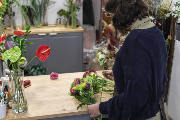 エプロン、若い女性起業家の概念を身に着けている彼女の花屋で緑と紫の花束を設計する女性のビュー。 - orchid flower single flower green ストックフォトと画像