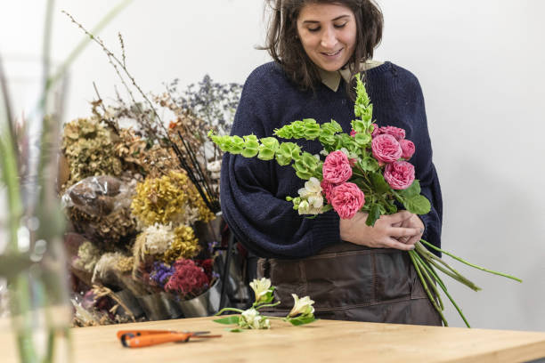 エプロン、若い女性起業家の概念を身に着けている彼女の花屋で緑と紫の花束を設計する女性のビュー。 - orchid flower single flower green ストックフォトと画像