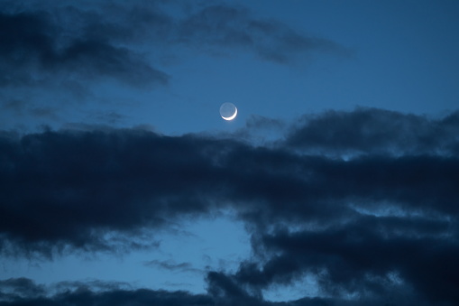 Night sky with dark clouds and a new moon.