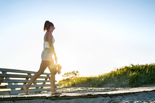 Summer evening walk on the beach boardwalk at dawn. Lonely sad young woman in melancholy or solitude at sunset. Almost silhouette of a person. Sunshine on a blue sky. Summer evening walk on the beach boardwalk at dawn. Lonely sad young woman in melancholy or solitude at sunset. Almost silhouette of a person. Sunshine on a blue sky. Morning sunrise on a holiday. walking beach women sadness stock pictures, royalty-free photos & images