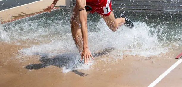 A high school boy running in a steeplechase race is falleing as he is trying too exit the water.
