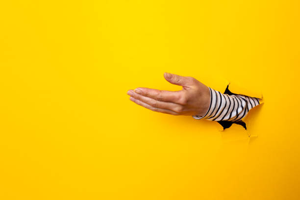 istock female hand palm in a hole on a torn yellow background 1319442621