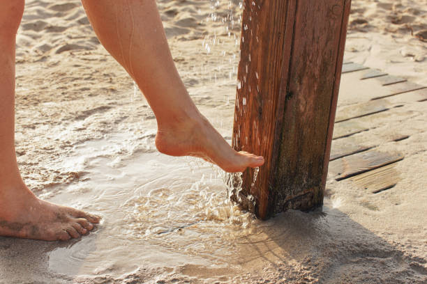 모래를 제거하는 젊은 여성은 모래 땅 근처 해변 샤워 에서 그녀의 다리를 형성, 물 방울은 발에 살포 - human leg women shower water 뉴스 사진 이미지