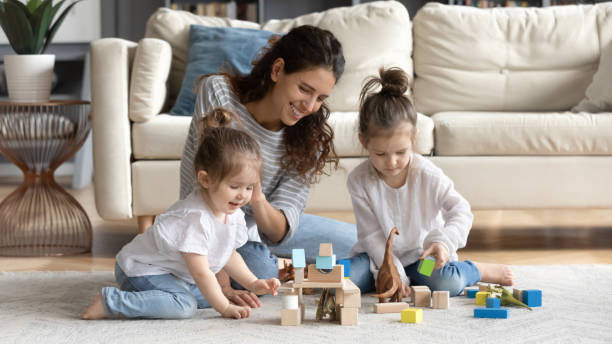 Caring happy mom play with little daughters Happy caring young Caucasian mother have fun play with small daughter at home in living room. Smiling loving mom feel playful engaged in game activity with blocks bricks with little girls children. nanny photos stock pictures, royalty-free photos & images