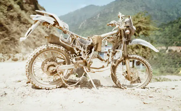 Abandoned old motocross Motorcycle be drowned in deep road dust near the crowed town road in Ramechhap, Nepal.