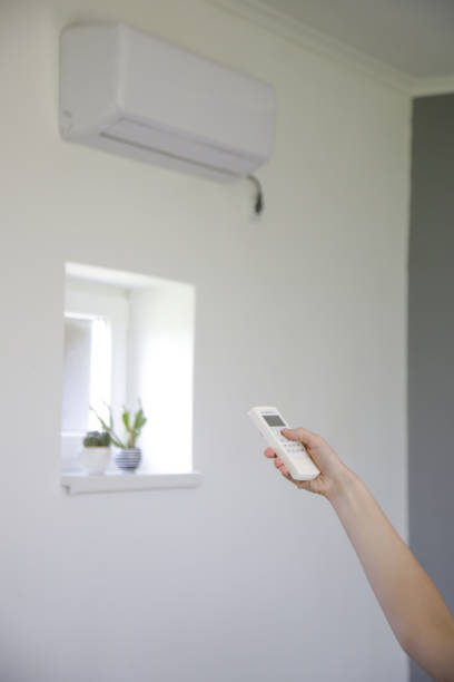 istock Human hand is using white remote of air conditioner to adjust temperature in a room. 1319452744