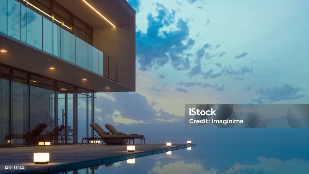 Modern Luxury House With Private Infinity Pool In Dusk Luxurious villa with private infinity pool and chaise lounges at summer in dusk. Luxury Stock Photo