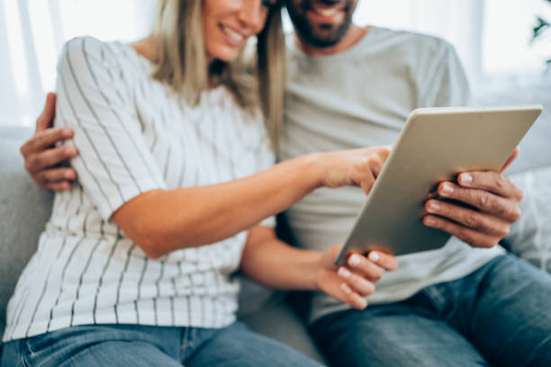 istock Smiling young couple using digital tablet at home. Focus is on the tablet. 1319457053