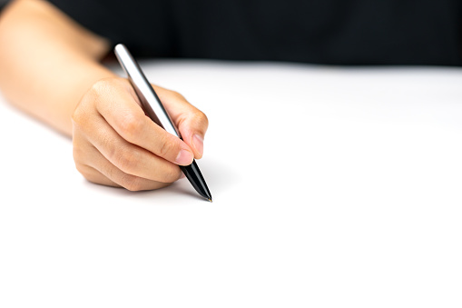 A woman holding a fountain pen in her hand is writing on white paper, focus on her hand, with the space for your own text message.