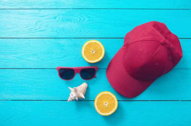 istock Summer accessories. Cap, sunglasses, shell and oranges on blue wooden background. Top view and copy space 1319457578
