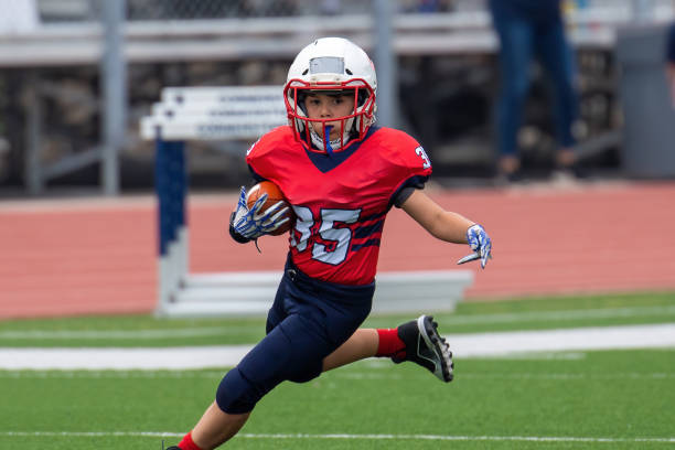 Athletic Young Boy Playing in a Football Game Athletic Football player catching and running with the ball during a game american football player stock pictures, royalty-free photos & images