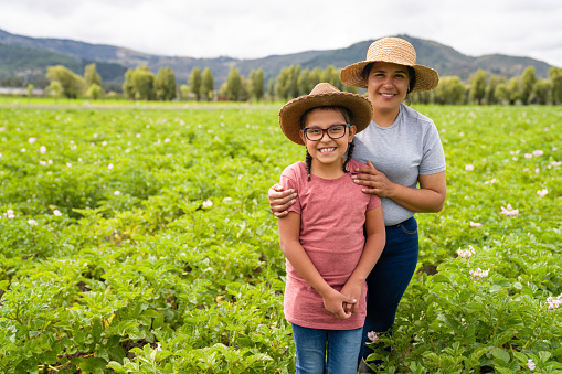Portrait of a happy Latin American mother and daughter working on agriculture at a farm and looking at the camera smiling - lifestyle concepts