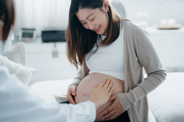 colpo ritagliato di donna incinta asiatica che ha avuto una consulenza con il medico durante il controllo di routine in clinica. il medico sta eseguendo un esame e toccando la pancia. controlli, test e scansioni per garantire una gravidanza sana sia per la - abdomen gynecological examination women loving foto e immagini stock