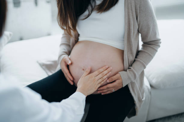 abgeschnittene aufnahme von asiatischer schwangerer, die während der routineuntersuchung in der klinik eine konsultation mit dem arzt hat. arzt führt eine untersuchung durch und berührt den bauch. check-ups, tests und scans, um eine gesunde schwangersch - human pregnancy midwife visit healthcare and medicine stock-fotos und bilder