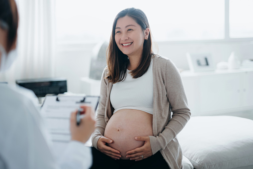 Mujer embarazada asiática sonriente que tiene una consulta con una doctora durante su chequeo de rutina en una clínica. Chequeos, pruebas y exploraciones para asegurar un embarazo saludable tanto para la madre como para el feto. Estilo de vida saludable  photo