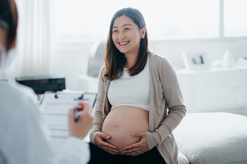 Smiling young Asian pregnant woman having a consultation with a female doctor during her routine check up at a clinic. Check-ups, tests and scans to ensure a healthy pregnancy for both mother and the unborn baby. Healthy pregnancy lifestyle