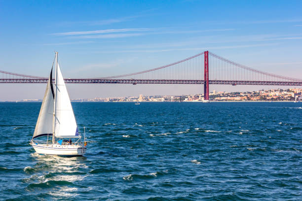 Sailboat close to April 25th Bridge over the Tagus river, Lisbon, Portugal stock photo