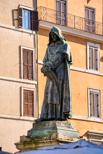 The severe gaze of the bronze statue of the religious and philosopher Giordano Bruno in Campo de Fiori square, located in the Baroque heart of Rome between Piazza Farnese and Piazza Navona. Made by the sculptor Ettore Ferrari in 1889, this statue was erected in the place where Giordano Bruno was condemned to the stake by the Holy Inquisition in 1600. Campo de Fiori in one of the most visited districts of the Eternal City, with ancient and noble palaces in warm pastel shades , baroque churches with countless artistic treasures, typical restaurants and trendy pubs, alleys and large pedestrian areas. Image in high definition format.