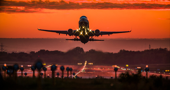 Passenger jet airplane taking off at sunset. Beautiful sky with dramatic red clouds.