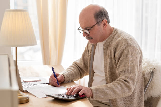istock Senior man sitting with paperwork and using calculator while counting money 1319477955