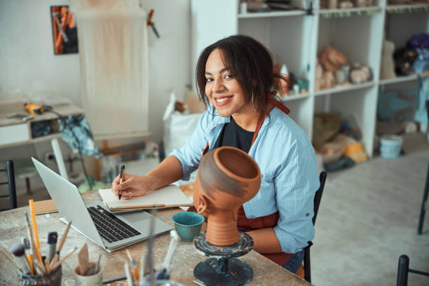 istock Cheerful woman ceramist using laptop and writing on notebook 1319479719