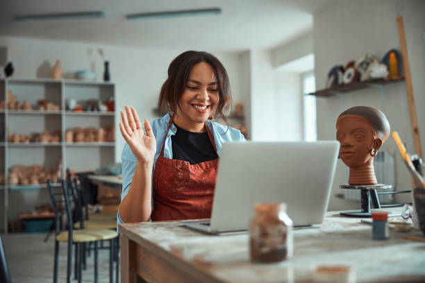 istock Cheerful female potter using laptop in pottery workshop 1319481645
