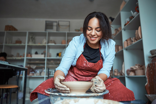 Cheerful young woman polishing pottery in workshop
