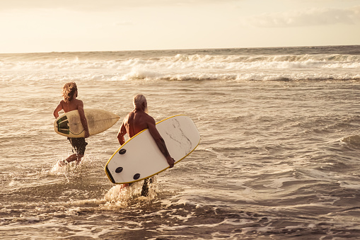 Friends going to surf on the beach at sunset. Father and son having fun doing extreme sport. Image