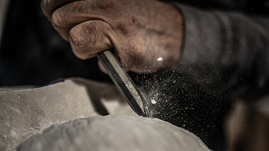 Close-up photo of a stonemasons hand as he uses a hammer and chisel on a stone.