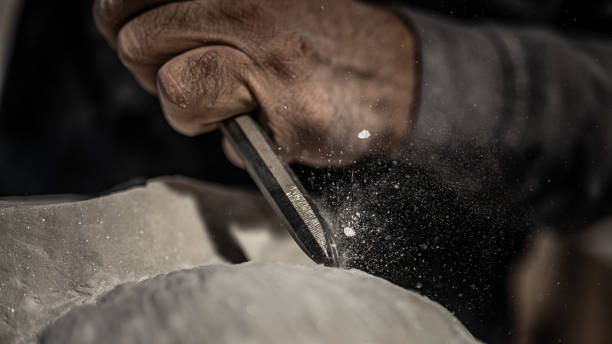 Close-up of a sculptor's hand as he chisels a stone Close-up photo of a stonemasons hand as he uses a hammer and chisel on a stone. chisel photos stock pictures, royalty-free photos & images