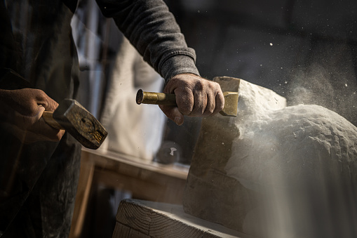 Close-up photo of a stonemason using a hammer and chisel to shape a piece of stone.