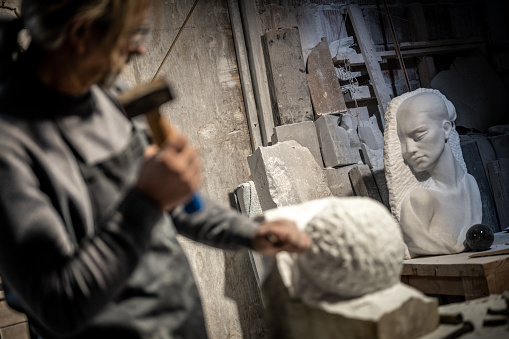 Stone sculptor in his workshop using a hammer and chisel to shape a piece of rock.