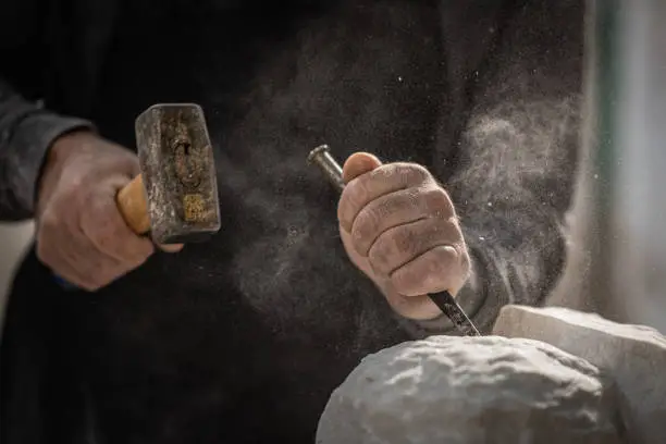 Close-up photo of a stonemason using a hammer and chisel to shape a piece of stone.