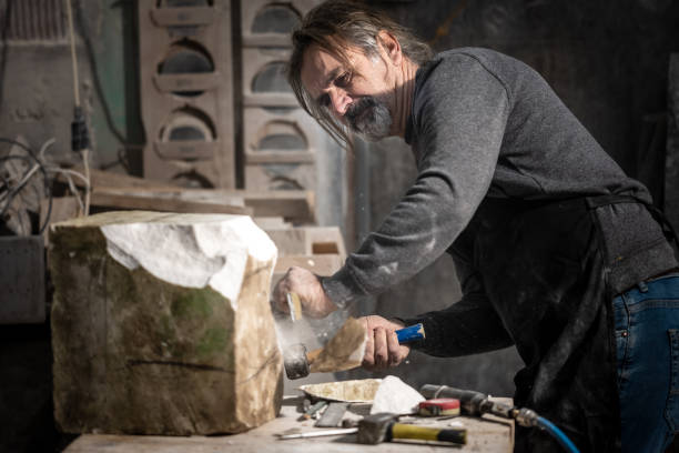 istock Caucasian stonemason shaping a rock with a hammer and chisel 1319483981