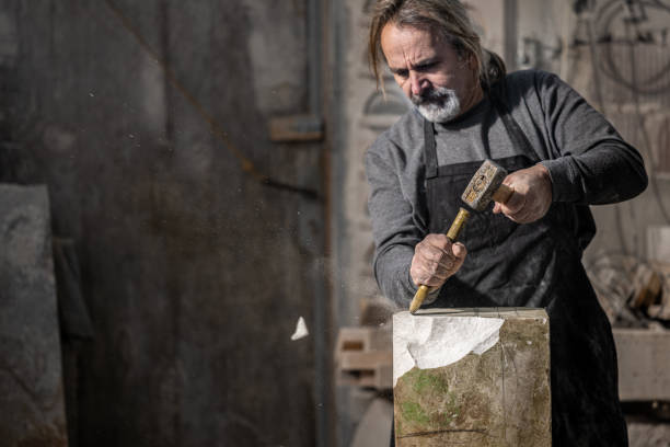 istock Caucasian stonemason shaping a rock with a hammer and chisel 1319483984