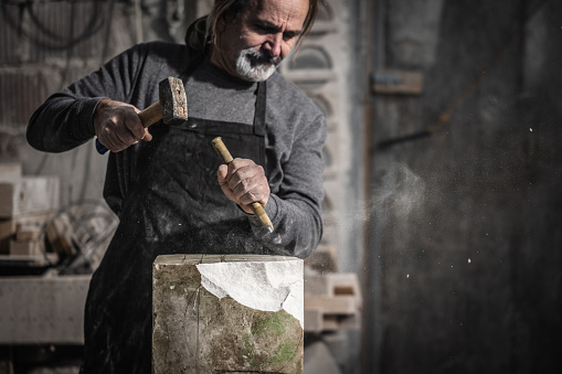 Sculptor chiseling a piece of rock with a hammer and chisel in his art studio.
