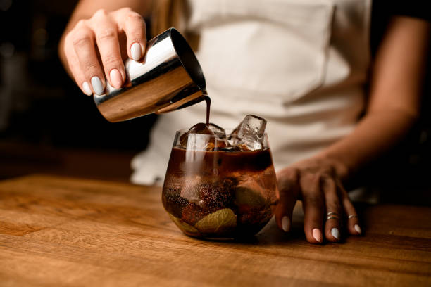 woman's hand holds steel cup and pours coffee into bowl with cold herbal drink - espresso women cup drink imagens e fotografias de stock