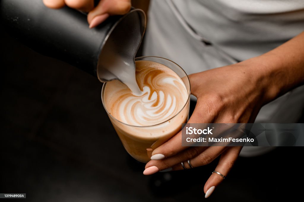 Close-up of woman who beautiful drawing pattern pouring milk into glass with latte Close-up of woman who beautiful drawing pattern pouring milk into glass with latte in her hand Froth Art Stock Photo