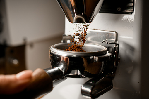 Close-up of portafilter in hands of barista into which coffee grinder pours ground coffee